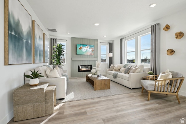 living area with visible vents, baseboards, recessed lighting, a large fireplace, and light wood finished floors