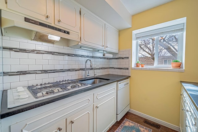 kitchen with under cabinet range hood, white appliances, a sink, visible vents, and tasteful backsplash