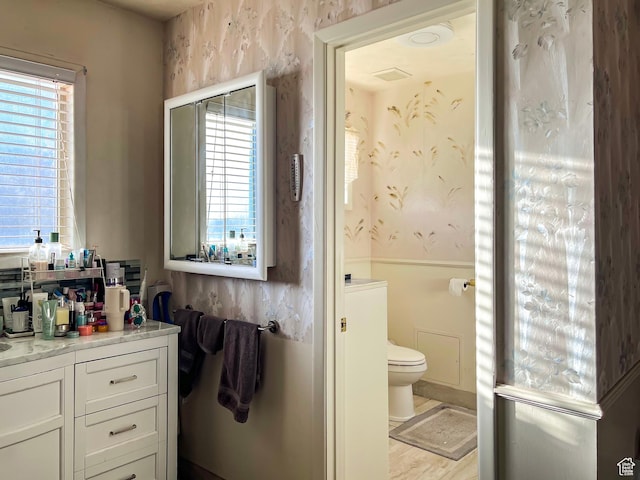 bathroom with a healthy amount of sunlight, vanity, toilet, and wallpapered walls
