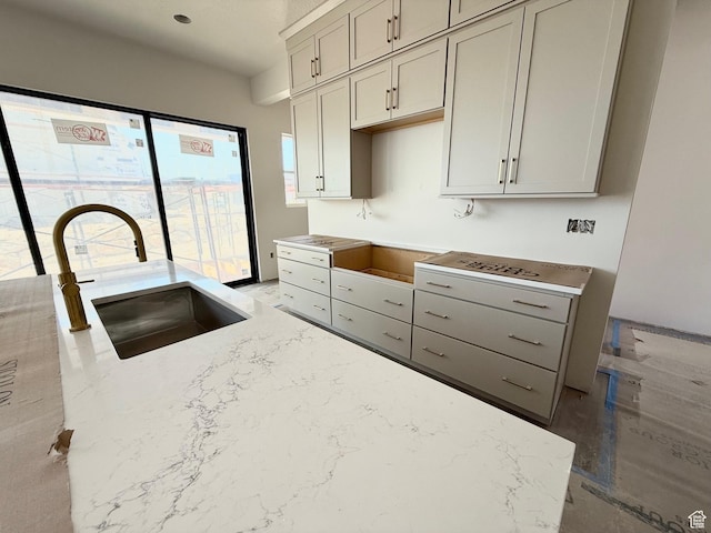 kitchen featuring a sink, light stone counters, and gray cabinetry