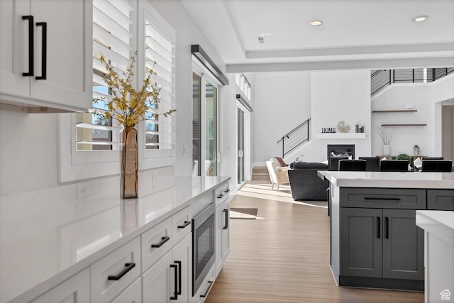 219 W Elinor Ln, Washington, UT 84780 - kitchen with light countertops, stainless steel microwave, gray cabinetry, a glass covered fireplace, and light wood-type flooring