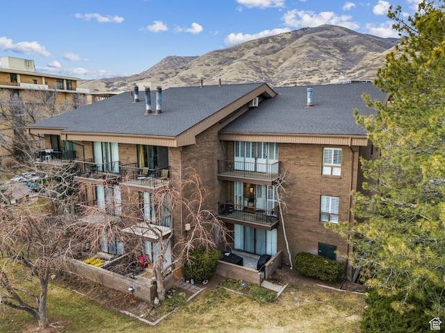 back of house featuring a shingled roof, brick siding, and a mountain view