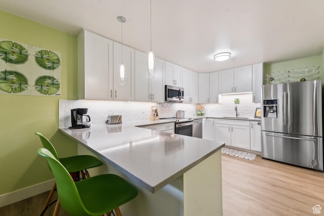 kitchen featuring stainless steel appliances, a peninsula, a sink, a kitchen breakfast bar, and decorative backsplash