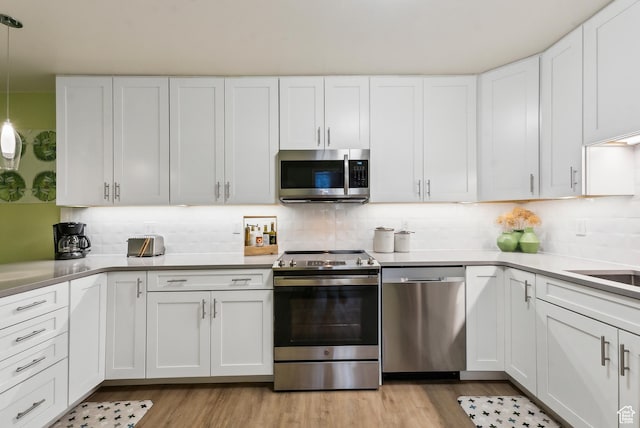 kitchen featuring stainless steel appliances, white cabinets, light wood-style flooring, and tasteful backsplash