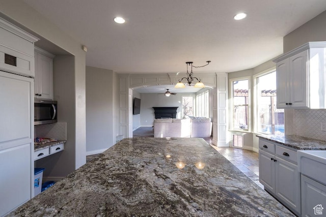 kitchen featuring a fireplace, tasteful backsplash, stainless steel microwave, dark stone countertops, and paneled built in refrigerator