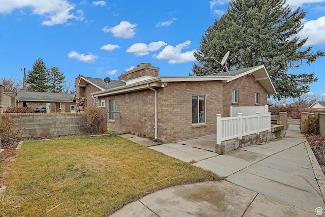 8693 S Vaquero Dr, Sandy, UT 84094 - view of home's exterior with brick siding, fence, a chimney, a yard, and a patio