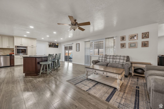 living room with wood finished floors, baseboards, recessed lighting, ceiling fan, and a textured ceiling