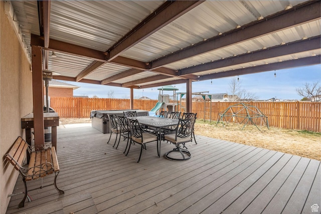 deck featuring a playground, outdoor dining area, and a fenced backyard