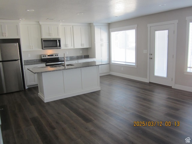 kitchen with stone countertops, stainless steel appliances, an island with sink, and white cabinetry