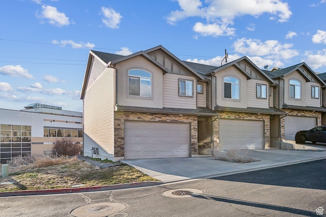 townhome / multi-family property featuring driveway, stone siding, a shingled roof, and a garage