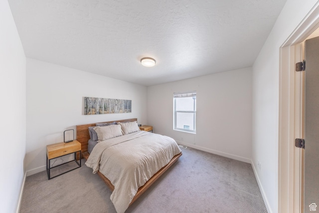 bedroom featuring light colored carpet, a textured ceiling, and baseboards