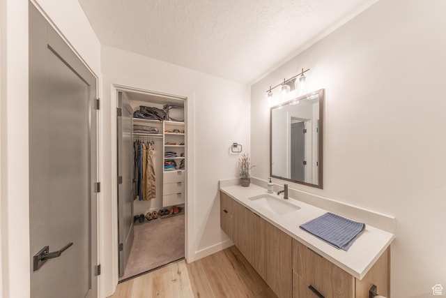 bathroom featuring a textured ceiling, wood finished floors, vanity, baseboards, and a spacious closet