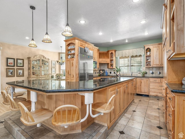 kitchen with open shelves, stainless steel built in refrigerator, decorative backsplash, a textured ceiling, and a kitchen breakfast bar