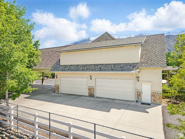 view of side of property featuring stone siding, stucco siding, fence, and driveway
