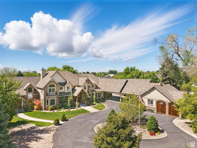 view of front of home featuring stone siding, curved driveway, a chimney, and fence