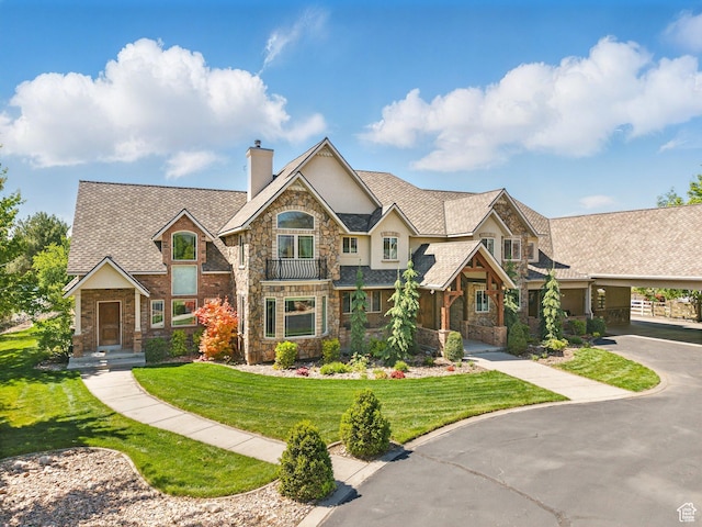 view of front of house with stone siding, a chimney, stucco siding, a front lawn, and driveway