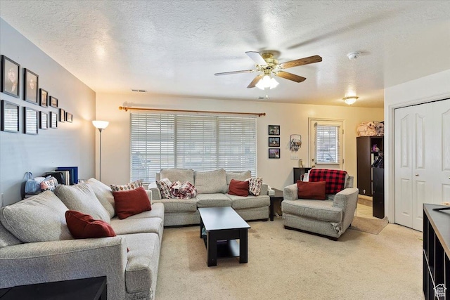 living area featuring a ceiling fan, a textured ceiling, light colored carpet, and visible vents