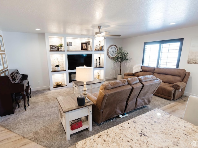 living area with built in shelves, ceiling fan, a textured ceiling, wood finished floors, and baseboards
