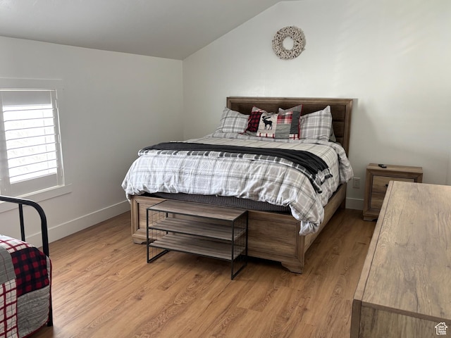 bedroom with lofted ceiling, light wood-style flooring, and baseboards