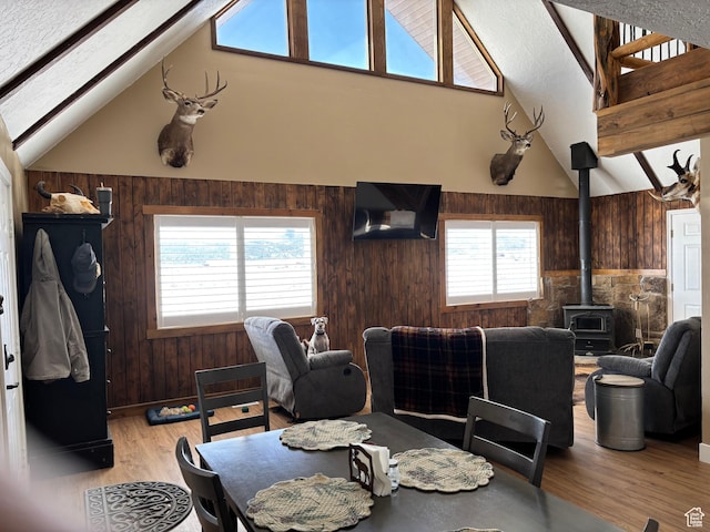 dining area with lofted ceiling with beams, light wood-type flooring, a wood stove, and wooden walls