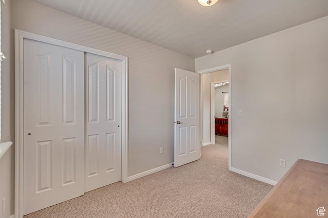 unfurnished bedroom with baseboards, light carpet, and a closet