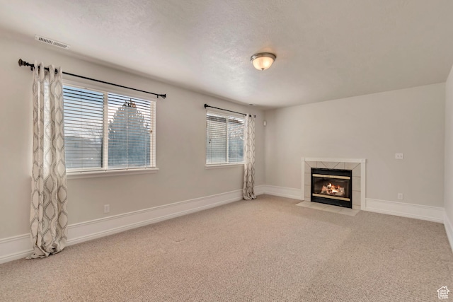 unfurnished living room with visible vents, a tile fireplace, baseboards, and carpet floors