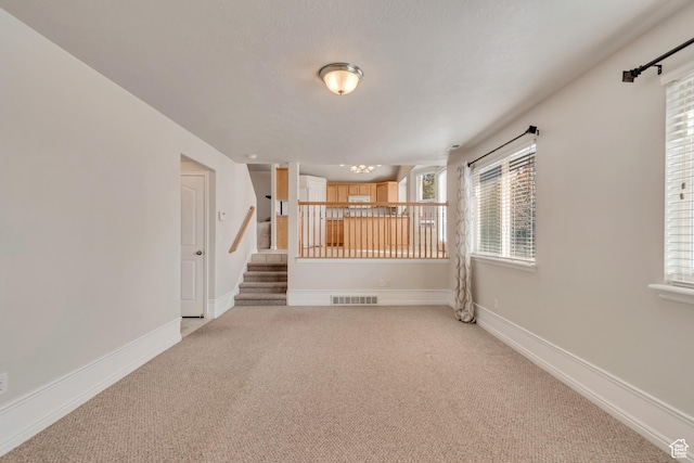 unfurnished room with visible vents, light carpet, baseboards, and stairs
