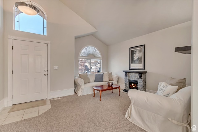 living area with light tile patterned floors, baseboards, a stone fireplace, vaulted ceiling, and light colored carpet