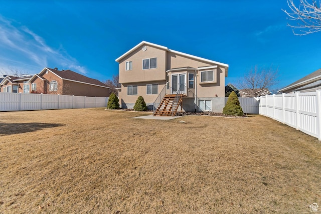 rear view of house with stucco siding, a lawn, entry steps, a fenced backyard, and french doors