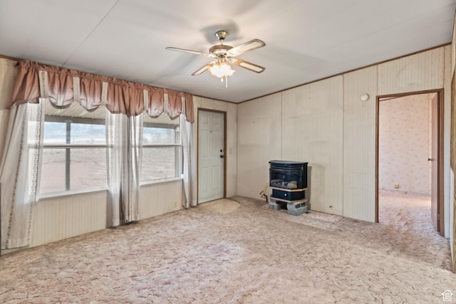 carpeted spare room featuring ceiling fan and a wood stove