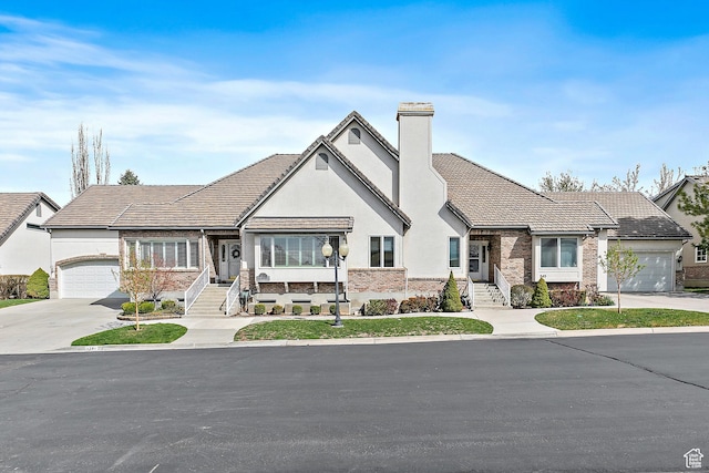 tudor home with a chimney, a garage, stucco siding, brick siding, and driveway