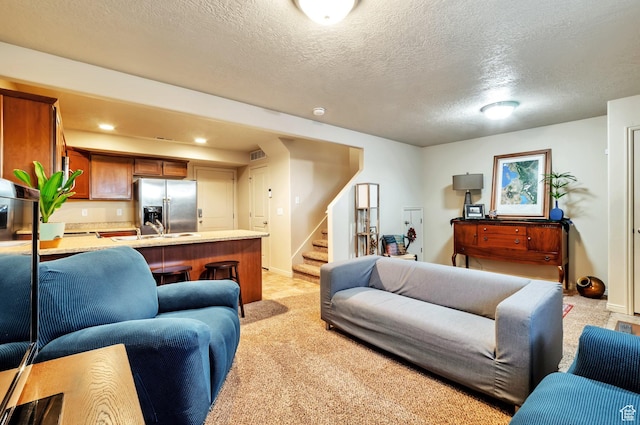 living area featuring visible vents, baseboards, stairs, a textured ceiling, and light carpet