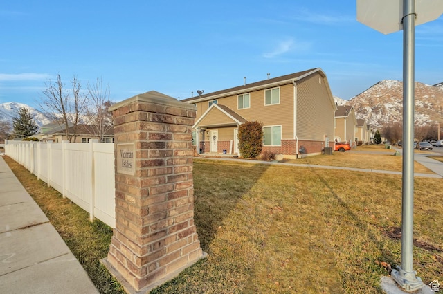 view of front of property with a mountain view, brick siding, a front lawn, and fence