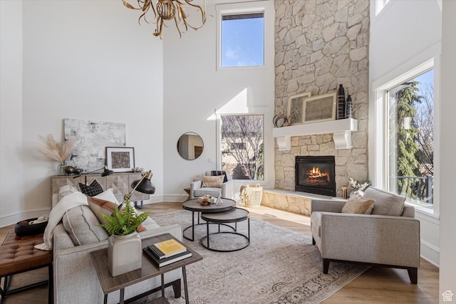 living area with a high ceiling, a stone fireplace, a wealth of natural light, and a chandelier