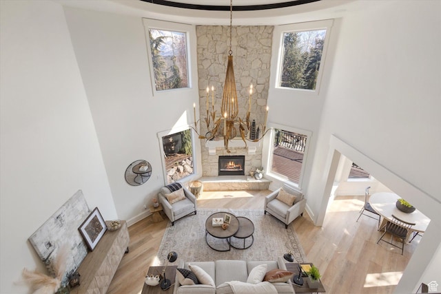 living area with a towering ceiling, baseboards, a notable chandelier, wood finished floors, and a fireplace