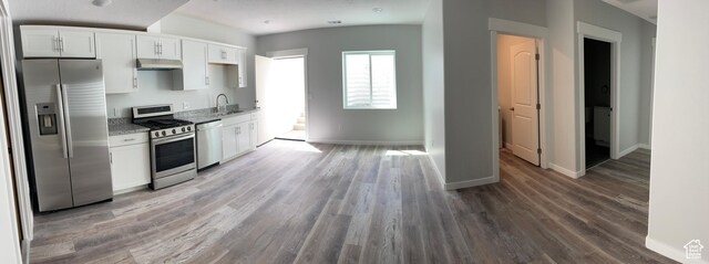 2421 S Blue Water Ln E, Saratoga Springs, UT 84045 - kitchen with light wood-style flooring, white cabinetry, under cabinet range hood, stainless steel appliances, and baseboards