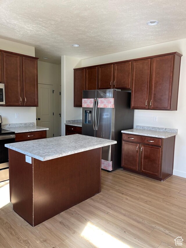 2421 S Blue Water Ln E, Saratoga Springs, UT 84045 - kitchen featuring light wood-style flooring, a textured ceiling, a center island, light countertops, and stainless steel appliances