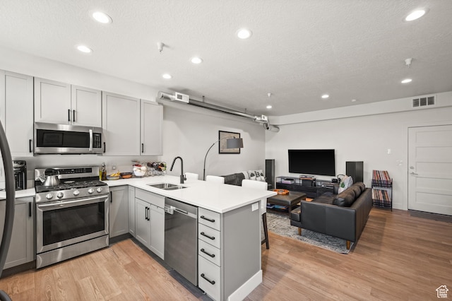kitchen featuring visible vents, gray cabinets, a sink, stainless steel appliances, and a peninsula