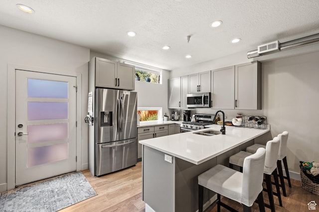 kitchen with a breakfast bar area, a peninsula, a sink, gray cabinetry, and stainless steel appliances