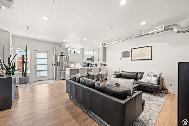 living area featuring light wood-style flooring, recessed lighting, visible vents, and a textured ceiling