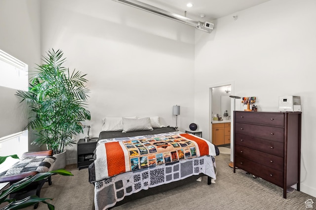 bedroom featuring light colored carpet, ensuite bathroom, and a towering ceiling