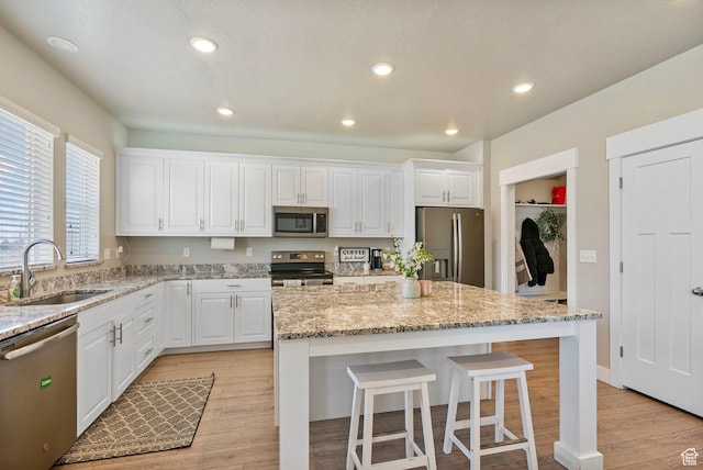 3323 E Gibraltar Ave, Eagle Mountain, UT 84005 - kitchen with a sink, white cabinets, appliances with stainless steel finishes, a kitchen bar, and light wood-type flooring