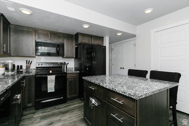 kitchen with light stone counters, dark wood-style floors, black appliances, and a breakfast bar area