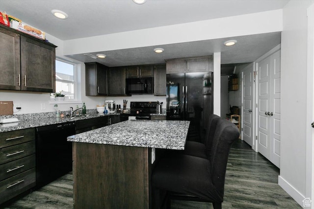 kitchen featuring black appliances, a kitchen breakfast bar, dark wood finished floors, dark brown cabinetry, and light stone countertops