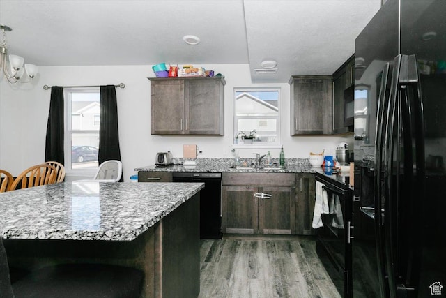 kitchen featuring light stone countertops, a sink, black appliances, dark brown cabinetry, and light wood-style floors