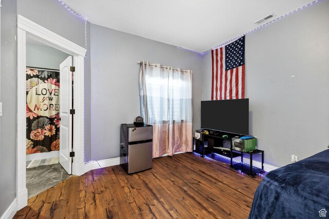 bedroom with wood finished floors, visible vents, freestanding refrigerator, and baseboards