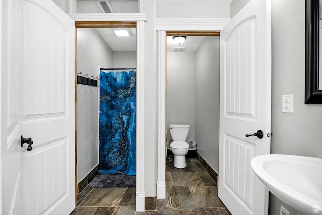 full bath with toilet, stone finish floor, a sink, curtained shower, and baseboards
