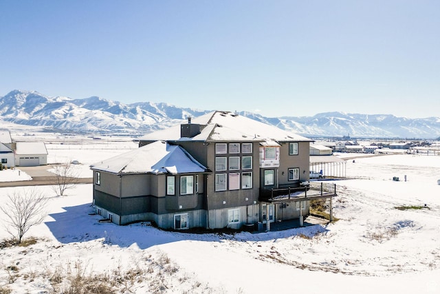 snow covered back of property with a mountain view and a chimney