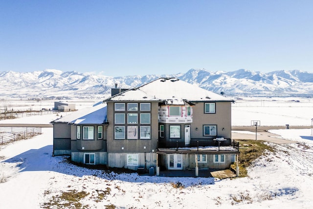 snow covered property featuring french doors, a mountain view, and stucco siding