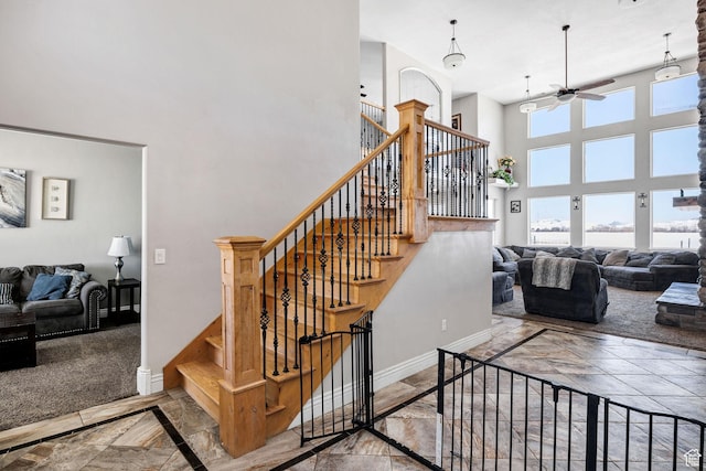 staircase featuring baseboards, marble finish floor, ceiling fan, and a towering ceiling